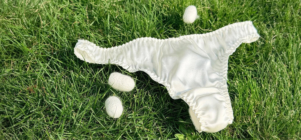 White silk underwear resting on green grass beside silk cocoons